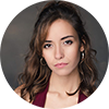 Carmen Lorenzo, A woman with brown curly hair, silver hoop earrings, and a serious expression in front of a gray backdrop
