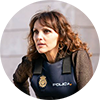 Ines Villegoes, a woman with curly brown hair wearing a police vest, with a serious expression, looking off to the right