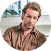 Max Winter, a man with short, dark blonde hair and a beard with a subtle smirk wearing a tan button down shirt